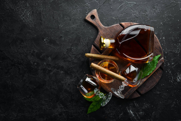 Brandy in glasses and cigars on a black stone table. Top view. Free space for your text. - Photo, Image