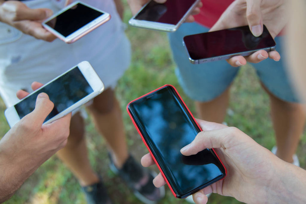 closeup of hands of young friends or students grouped with mobile phones outdoors - Photo, Image