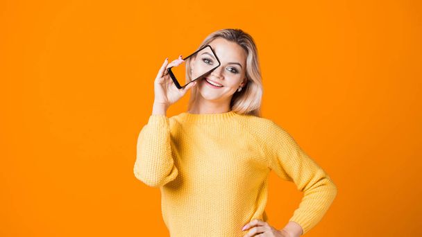 young blonde in a yellow sweater holds a smartphone in her hand with her selfie on the screen. - Photo, Image