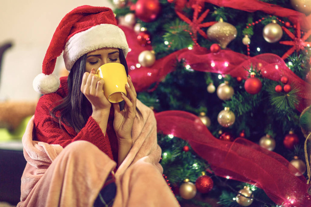 Різдво і Новий рік. Жінка в капелюсі Санти тримає чашку гарячого чаю
 - Фото, зображення