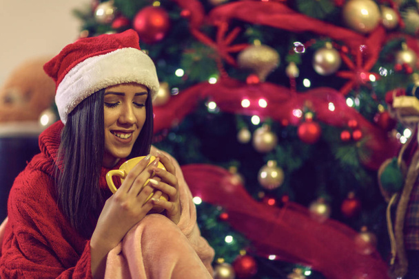  Усміхнена жінка п'є чашку чаю напередодні Різдва
 - Фото, зображення