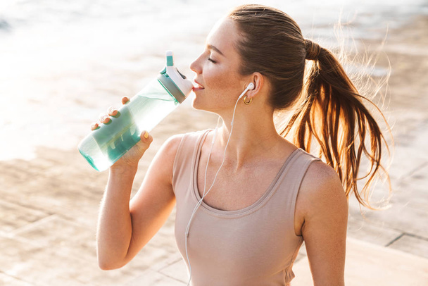 Sports woman outdoors on beach drinking water - Foto, imagen