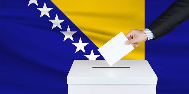 Выборы в Боснии. Рука человека, положившего свой голос в урну для голосования. Флагом Боснии на заднем плане
. - Фото, изображение