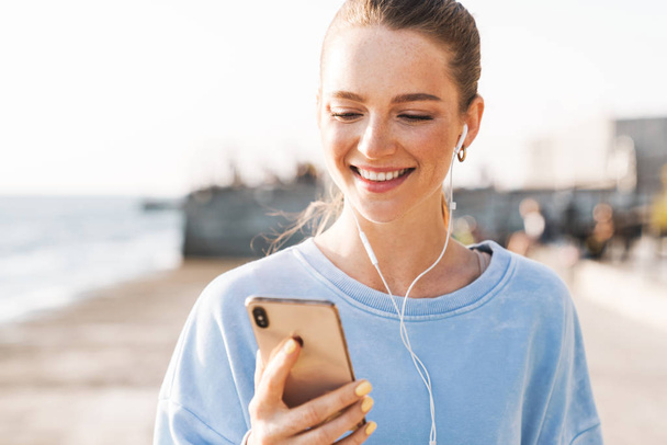Positive young fitness woman outdoors listening music - 写真・画像