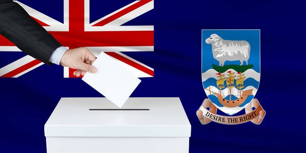 Eleição nas Ilhas Malvinas. A mão do homem a pôr o seu voto nas urnas. Bandeira das Ilhas Falkland ondulada no fundo
.                                - Foto, Imagem