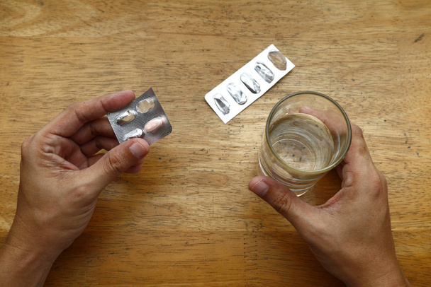 Пустая упаковка с лекарствами на столе и рука с стаканом воды
 - Фото, изображение