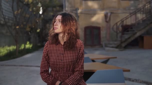 Dreaming young woman with spectacular curly red ginger hair looking at camera posing outdoor in downtown street. Female portrait. - Materiał filmowy, wideo