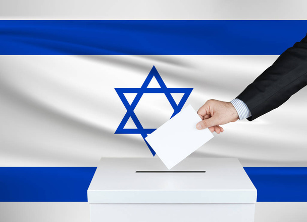 Vaalit Israelissa. Miehen käsi, joka laittaa äänensä vaaliuurnille. Heilutti Israelin lippua taustalla
.                                - Valokuva, kuva