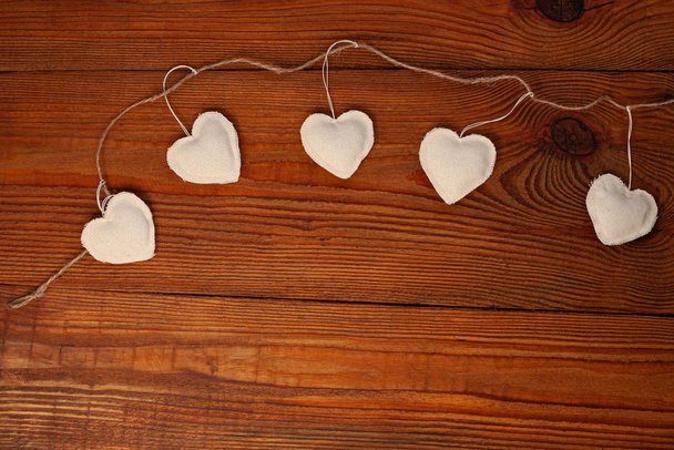 Екологічні серця лляної тканини на дерев'яному тлі, дизайн концепції Дня Святого Валентина. Декоративне біле серце на джутовій гірлянді
. - Фото, зображення