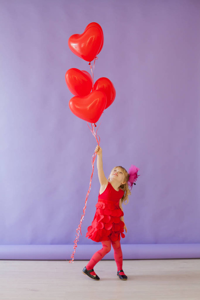 Beautiful little girl with red balloons in the shape of a heart - Foto, Imagen