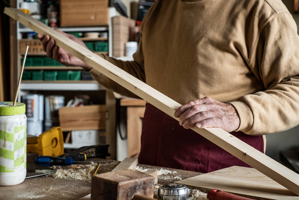 Плотник смотрит на деревянную доску в столярной мастерской
 - Фото, изображение