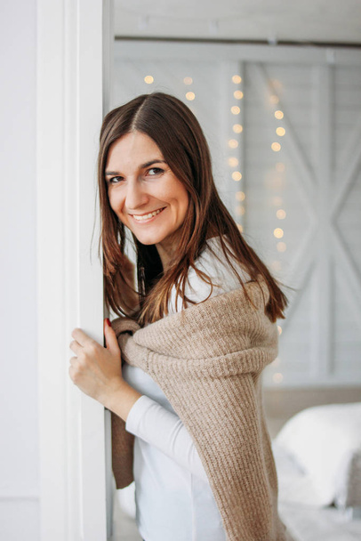 Beautiful smiling young woman dark long hair girl wearing in cozy knitted cardigan looking from door at home - Photo, Image