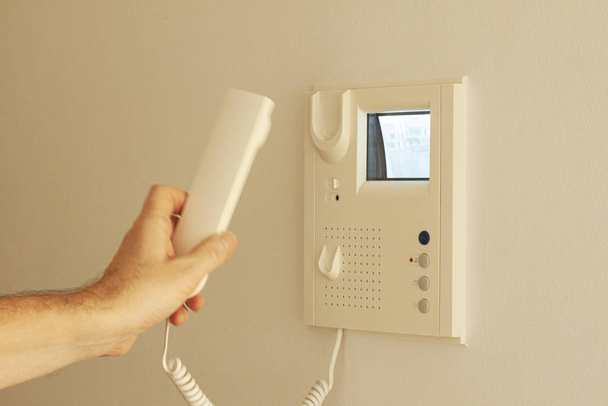 Video door phone with image on CRT display hanging on a wall. Hand holding handset. Video intercom equipment.  Selective focus image. - Фото, изображение