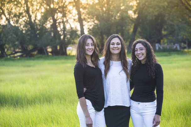 Horizontal Outdoor Portrait of three beautiful Hispanic young women standing together outdoors. Smiling and looking at a camera - Valokuva, kuva