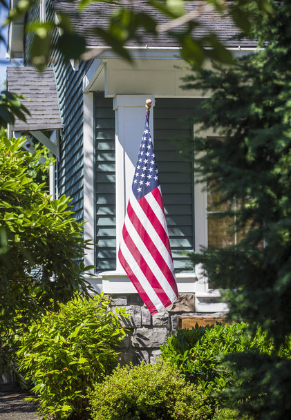 近所の家の前にアメリカ国旗が吊るされている。縦の写真とフラグに選択的な焦点 - 写真・画像