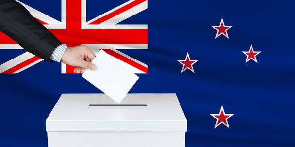 Wybory w Nowej Zelandii. Ręka człowieka oddającego głos w urnie wyborczej. Pomachał flagą Nowej Zelandii na tle.                                - Zdjęcie, obraz