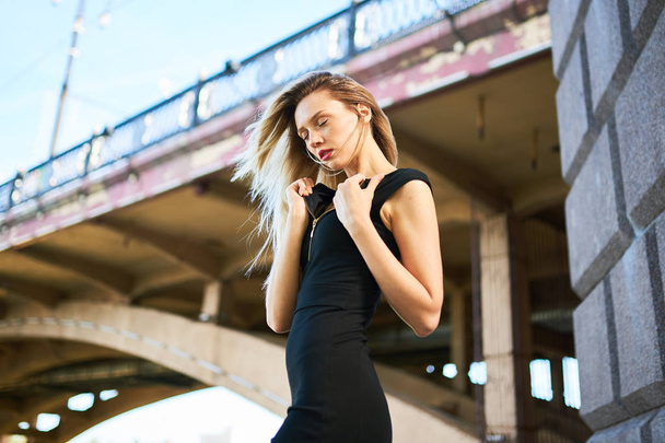 Sexy blonde girl in a black dress. Against the background of an arched bridge. - Фото, зображення