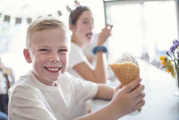 Lächelnde Kinder genießen Eiszapfen in einer Eisdiele. Kleiner Junge mit Waffelkegel genießt leckeres Eis - Foto, Bild