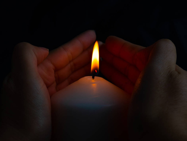 Hand protecting candle light from the wind in darkness - Фото, изображение
