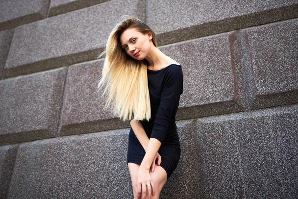 Atractiva rubia con un vestido negro. Sobre el fondo de un muro de piedra
. - Foto, Imagen