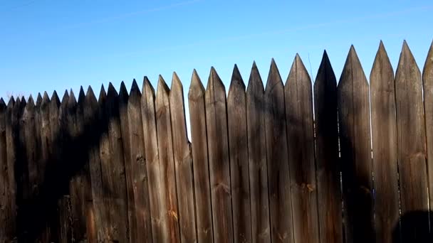 Omheining gemaakt van scherpe houten palen, blauwe heldere lucht, zonnige dag - Video
