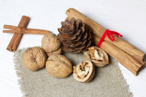 Walnuts, cinnamon sticks and fir cone. Lying on a piece of linen. Against the background of white painted boards. - Foto, imagen
