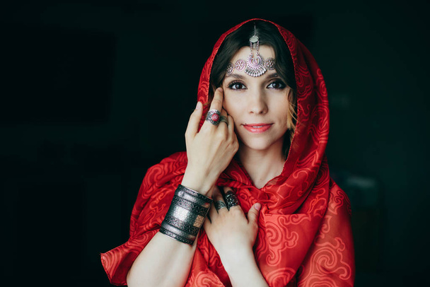 Oriental portrait of beautiful woman wearing jewellery and   red palatine  - Foto, afbeelding