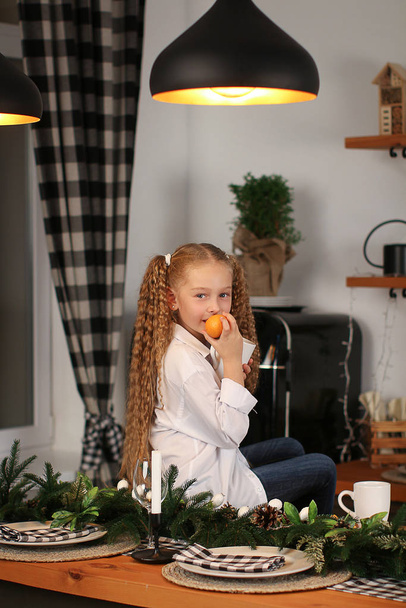 Malá krásná dívka slaví Nový rok sedí na stole s šálkem horkého čaje na pozadí okna se světly - Fotografie, Obrázek