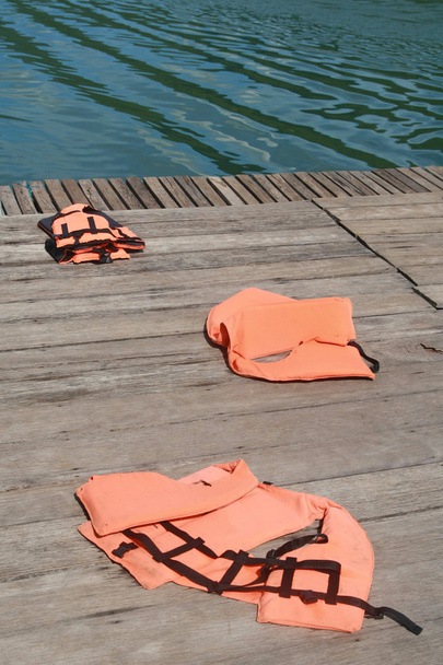 Záchranná vesta na dřevěnou podlahu s lodí na řece pozadí - Fotografie, Obrázek