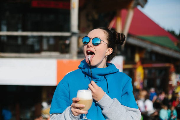Young woman snowboarder wearing sunglasses drinking coffee from glass cap outdoor in Winter Ski resort  - 写真・画像