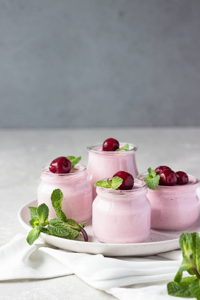 Delicious Italian dessert cherry panna cotta with fresh cherries and mint in jars. Light grey stone background, selective focus. Copy space. - Fotoğraf, Görsel