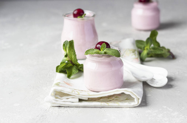 Delicious Italian dessert cherry panna cotta with fresh cherries and mint in jars. Light grey stone background, selective focus. Copy space. - Foto, immagini
