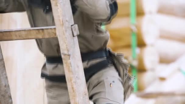 Close-up van een man met een overall op een houten ladder. Een knip. Professionele timmerman klimmend op een ladder op de bouwplaats. - Video