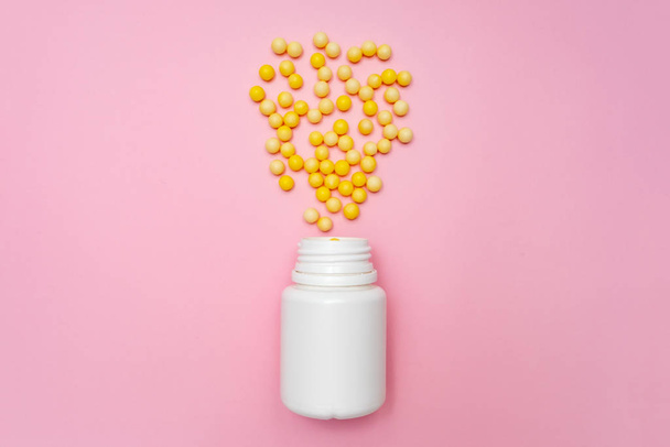 Yellow round dragees of vitamin c, ascorbic acid near a white plastic bottle, container on pink background - Fotografie, Obrázek