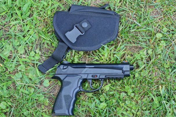 Egy fekete pisztoly egy pisztolytáskában fekszik a zöld fűben odakint. - Fotó, kép