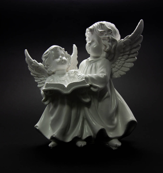 Suojelusenkeli tummalla pohjalla kaksi enkeliä lukee kirjaa
 - Valokuva, kuva