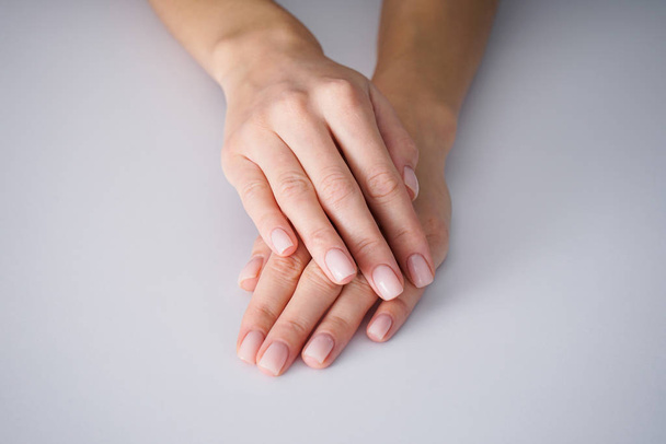 weibliche Hände mit einer schönen Maniküre auf grauem Hintergrund, nackt. - Foto, Bild
