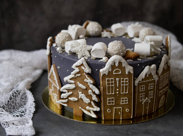 Christmas gray cake decoraited of gingerbread cookies in shape of homes and snowy christmas trees, marshmallows, snowflakes, sweets. Christmas, New Year greeting card. Gray background. Copy space. - Foto, Imagem