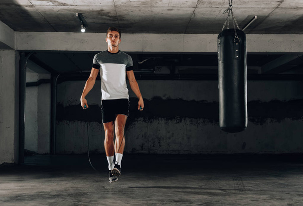 Portrait of a young sportsman in the sportwear skipping with a jumping rope - Фото, изображение