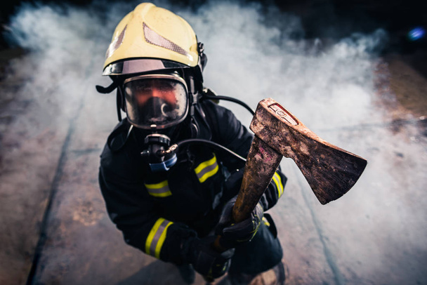 Retrato de una mujer bombero mientras sostiene un hacha y el desgaste
 - Foto, Imagen