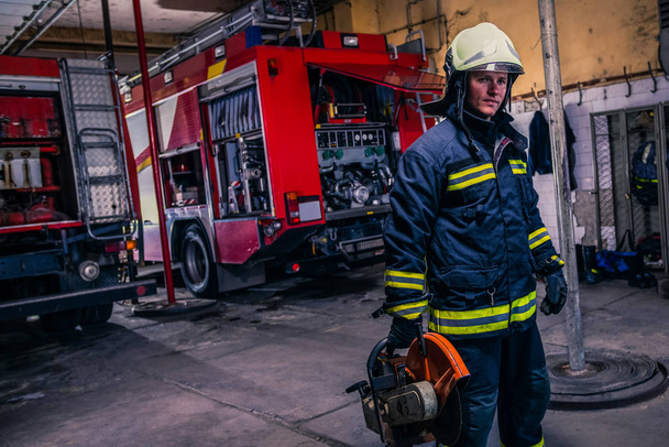 A fireman with uniform and helmet holding a chainsaw with fire t - Valokuva, kuva