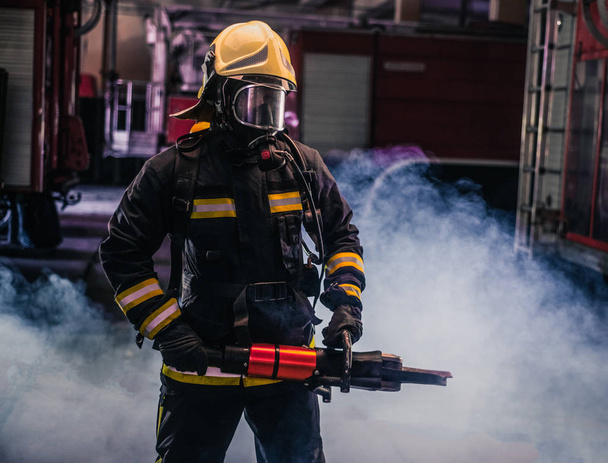 Портрет молодого пожарного, стоящего и держащего бензопилу в руках - Фото, изображение
