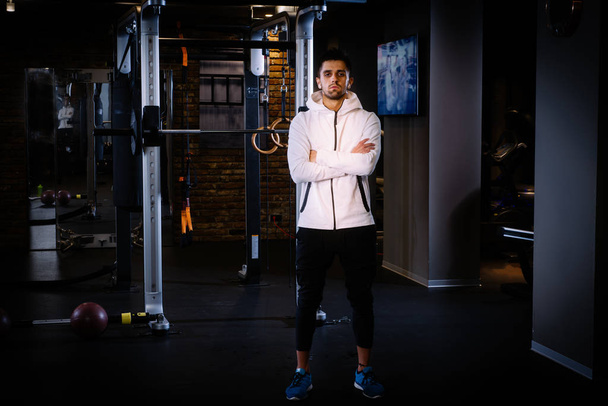 Karcsú izmos férfi áll büszkén edzés után a tornateremben, nagy kontrasztú kép. hosszú expozíciós mozgás elmosódás - Fotó, kép