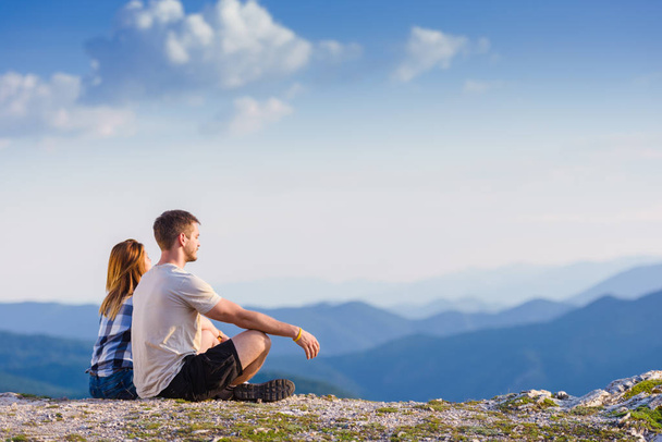 Enjoying the sun and the view from the mountain top. A couple enjoying the view on a peak of the mountain having a zen moment at sunset. Success, winners, zen, tranquility, meditation. - Foto, Imagen