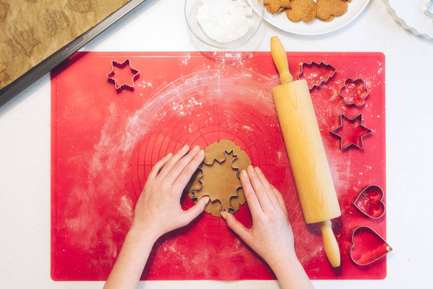 Рождественская пекарня. Женщина делает пряничные пряники, режет печенье из пряничного теста, вид сверху. Праздничное питание, кулинарный процесс, семейные кулинарные, рождественские и новогодние традиции
 - Фото, изображение