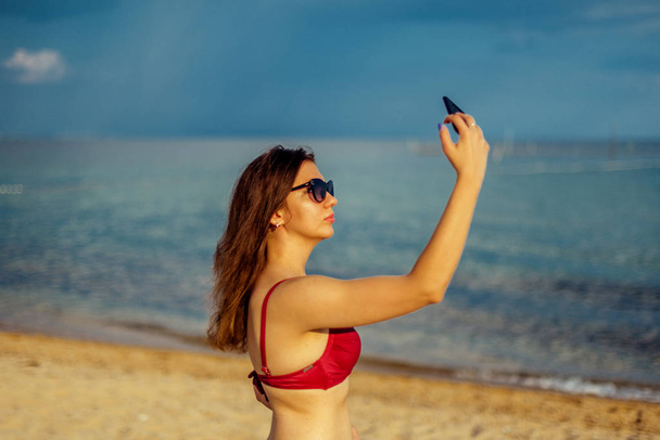 Young woman taking selfie on smartphone on beach - Fotoğraf, Görsel