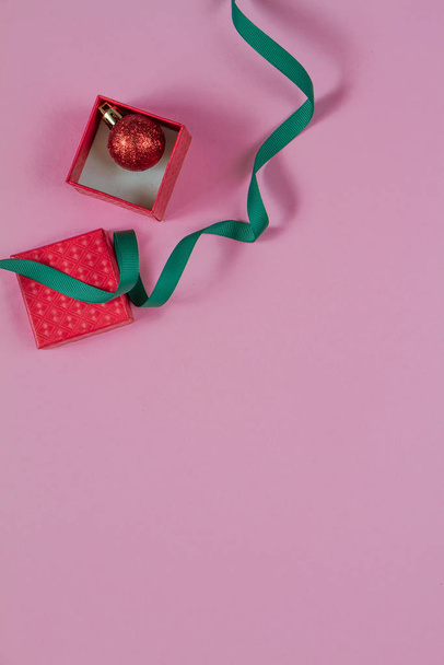 Открытая красная подарочная коробка и красный пузырь внутри с зеленой лентой на розовом изображении сверху стола. Плоский лежал. День рождения, свадьба или Рождество
. - Фото, изображение