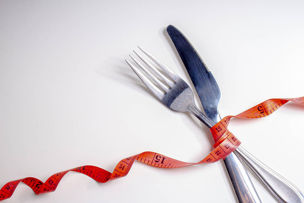 Perdere peso. Una forchetta e un coltello sono avvolti in un nastro di misurazione rosso su sfondo bianco su angolo tagliato
 - Foto, immagini