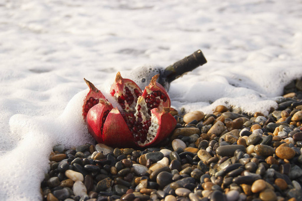 Érett gránátalma gyümölcs palack bor a strandon. Romantikus nap a tengerparton.  - Fotó, kép