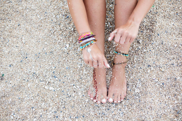 woman hand and feet with bracelets on sea beach - Foto, afbeelding